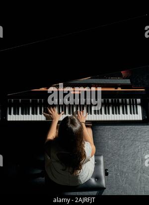 Une femme avec les cheveux bruns habillé en robe blanche vu jouer un piano à queue noir avec le couvercle soulevé. Vue de dessus de la pianiste à son corps et Banque D'Images