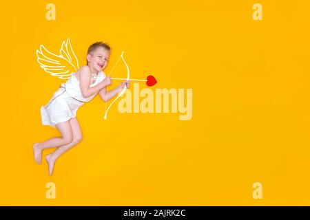 Happy smiling baby cupid en costume d'ailes d'ange, arc et flèche coeur jaune isolé sur fond de studio. Copyspace pour le texte. Valentines Day concept Banque D'Images