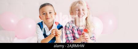 Heureux les enfants de race blanche en forme de coeur drôle de manger rouge lollipops. Meilleurs amis pour toujours. Maison de l'amour Saint Valentin concept. En-tête de bannières Web pour websi Banque D'Images