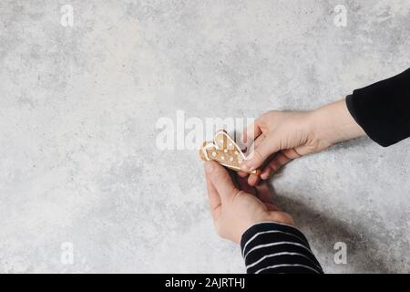 Femme et enfant mains tenant le pain d'épice coeur cookie avec glaçage blanc. Valentin ou la fête des mères, jour de composition. Concept d'amour. Grunge backg Banque D'Images