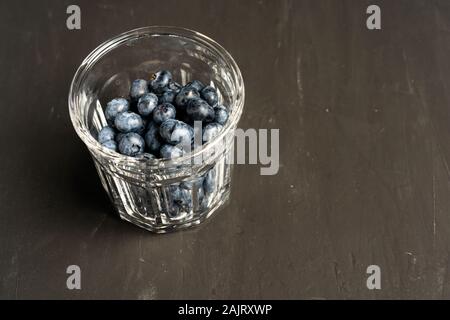 Belle matière savoureuse blueberry avec une tasse en verre transparent sur un fond en béton noir foncé. La vitamine D'une saine alimentation Banque D'Images