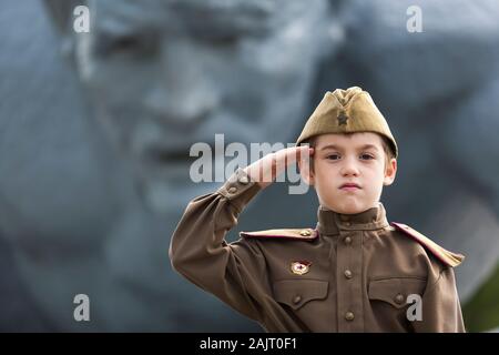 Un jeune garçon salue avec un regard fier et vêtu d'un uniforme de la seconde guerre mondiale et le Mémorial de Brest en Biélorussie Banque D'Images