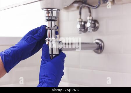 Plombier répare et entretient siphon chrome sous le lavabo. Plombier au travail dans la salle de bains, plomberie Montage et pose concept Banque D'Images