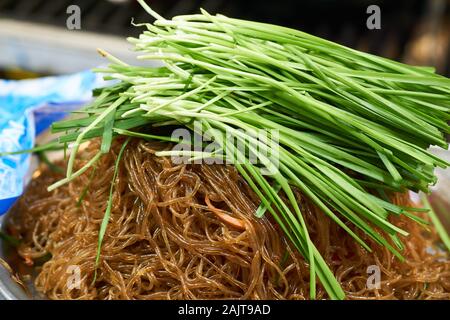 Nouilles sautées coréennes (japchae) recouvertes de nombreuses ciboulettes à l'ail vert frais à vendre au marché de Gwangjang à Séoul, en Corée du Sud. Banque D'Images