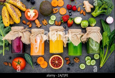 Des smoothies et des jus de fruits sains colorés dans des bouteilles avec des fruits tropicaux frais et l'air sombre sur fond de pierre avec l'exemplaire de l'espace. Banque D'Images