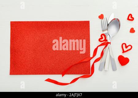 Fatigué de coutellerie par ruban rouge avec beaucoup de coeurs rouges à Jour de Valentines. Table de fête, sur une table en bois blanc. Dîner dans un restaurant. Valentin Banque D'Images