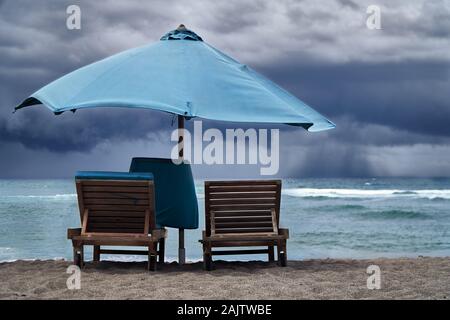 Tempête sur la mer avec des nuages orageux. Plage vide avec parasol et transats sur fond de pluie sur l'océan. Banque D'Images