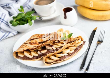 Crêpes français avec pâte à tartiner au chocolat et banane sur plaque blanche. Aliment sucré Banque D'Images