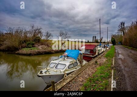 Vieux bateaux à moteur et de croiseurs amarré jusqu'à une digue au large de la Norfolk Broads sur un terne et nuageux jour d'hiver Banque D'Images