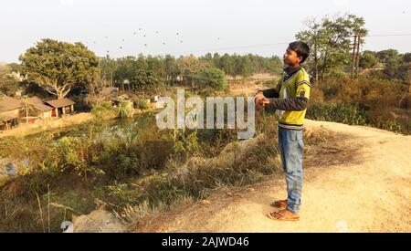 Bishnupur, Bengale de l'Ouest/Inde - 8 février 2018: Portrait d'un jeune garçon qui sourit tout en tenant l'axe avec des cordes de cerf-volant au sommet d'une colline. Banque D'Images