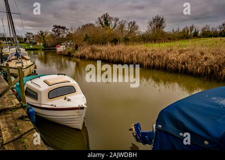 Vieux bateaux à moteur et de croiseurs amarré jusqu'à une digue au large de la Norfolk Broads sur un terne et nuageux jour d'hiver Banque D'Images