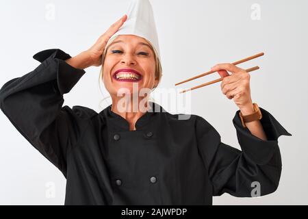 L'âge moyen chef woman wearing cap holding baguettes sur fond blanc isolé a souligné avec la main sur la tête, choqué par la honte et la surprise face, Banque D'Images