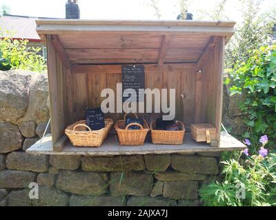 L'honnêteté et de l'honnêteté de décrochage fort sur un mur de jardin dans un village du Derbyshire la vente d'une variété de gâteaux faits maison avec un paiement en espèces à partir d'étain Banque D'Images