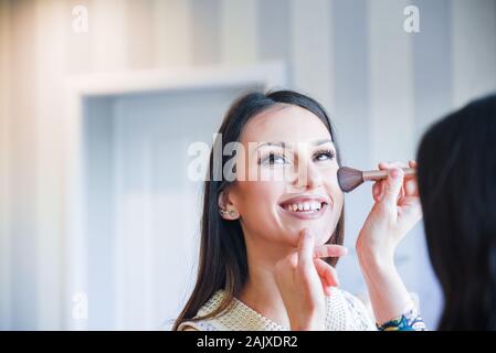 De session avec un entrepreneur de beauté féminine effectuant un pinceau précis se déplace sur une joue d'une belle jeune femme brunette model Banque D'Images