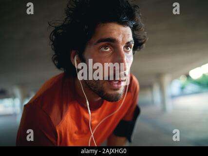 Portrait d'un jeune homme sérieux en sueur épuisé runner avec écouteurs dans ses oreilles se détendre après l'exécution à distance dans la Banque D'Images