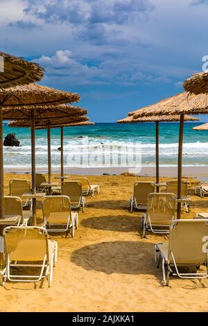 Destination vacances d'été. Les parasols de paille et de chaises longues sur la plage de galets vide avec la mer en arrière-plan. Vacances et Tourisme Concept. Transats O Banque D'Images