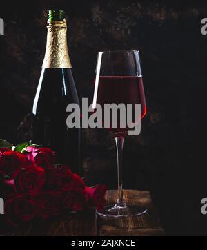 Dark définition d'un verre de vin et un bouquet de roses rouges avec une bouteille en arrière-plan sur une table en bois Banque D'Images