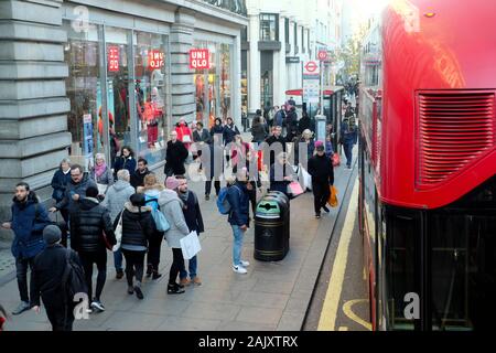 Les personnes portant des vêtements d'hiver shoppers debout en attente d'un bus à un arrêt de bus à l'extérieur de magasin Uniqlo dans Oxford Street London England UK KATHY DEWITT Banque D'Images