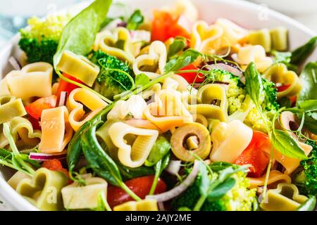 Valentine's Day food concept. Pâtes Salade de coeurs, olives, tomates, épinards et brocoli dans un bol blanc. Banque D'Images