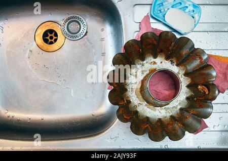 Seule la cuisson sale forme métallique. Les restes de cuisson douce. Placé sur le dessus d'un évier de cuisine en acier avec des gouttelettes d'eau tout autour. Gant rose Banque D'Images