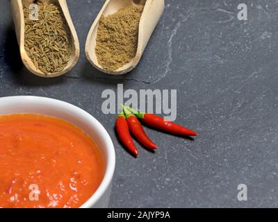 Vue de dessus gros plan de la sauce Harissa en cuvette ronde et à la coriandre, cumin romain et le piment sur la table en pierre sombre avec copie espace. Banque D'Images