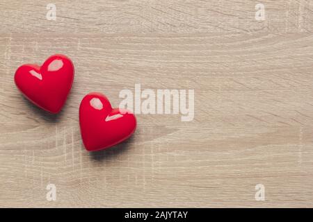 Stock photo de deux coeurs en plastique rouge sur un fond de bois. Le cœur sur le côté gauche avec un espace réservé au texte Banque D'Images