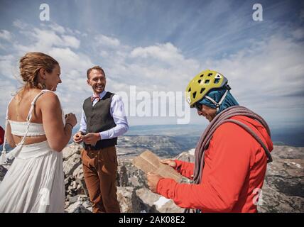 Un guide d'escalade avec casque lit les voeux lors du mariage au sommet d'une montagne Banque D'Images