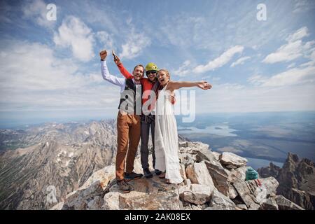 Jeunes mariés fêtent avec un guide d'escalade sur le sommet de la montagne Banque D'Images