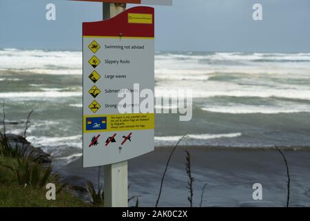 Un panneau avertissant les nageurs et les amateurs de plage de dangers dangereux à la plage de Muriwai, en Nouvelle-Zélande, l'une des plages les plus dangereuses en Nouvelle-Zélande. Banque D'Images