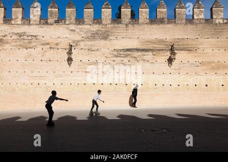 Deux garçons sur rollers et un passant dans l'après-midi paysage de murs de ville dans la région de Bab Mechouar et Bab Dekkakin à Fes (fez), Maroc Banque D'Images