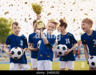 Heureux enfants dans l'équipe de sports de l'école primaire célébrant le succès du football dans le jeu final du tournoi. Trophée garçons souriant et levant la coupe d'or Banque D'Images