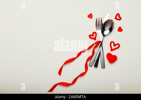 Fatigué de coutellerie par ruban rouge avec beaucoup de coeurs rouges à Jour de Valentines. Table de fête, sur une table en bois blanc. Dîner au restaurant Banque D'Images