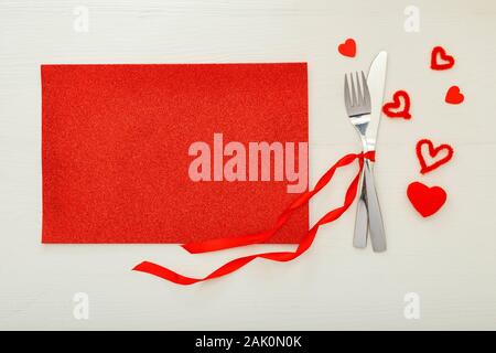 Fatigué de coutellerie par ruban rouge avec beaucoup de coeurs rouges à Jour de Valentines. Table de fête, sur une table en bois blanc. Dîner au restaurant Banque D'Images