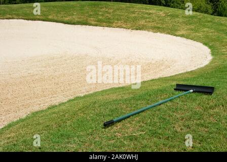 Fosse de sable ratissée récemment lors d'un parcours de golf avec le râteau couché dans l'herbe verte à côté. Banque D'Images