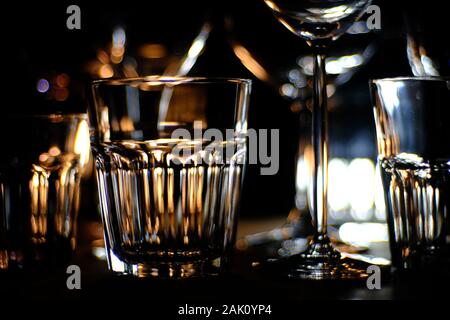 Gros plans de- vin, spiritueux et long drink--verres sur une étagère en bois dans un bar, en face d'un fond sombre, illuminé par spo colorés Banque D'Images