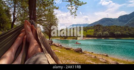 Couple reposant dans hamac (vue depuis hamac) sur la plage ensoleillée du lac de montagne, ciel bleu avec des nuages blancs Banque D'Images