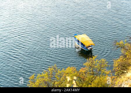 Bateau touristique bleu avec toit en toile jaune sur le lac d'Ohrid. Vue de dessus. Des arbres verts, sur la rive du lac. Ohrid, Macédoine, Europe du Nord. Banque D'Images