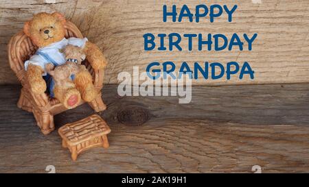 Ours en résine assis sur une chaise avec un chiot sur ses genoux sur un fond en bois naturel avec joyeux anniversaire papi message en texte bleu Banque D'Images