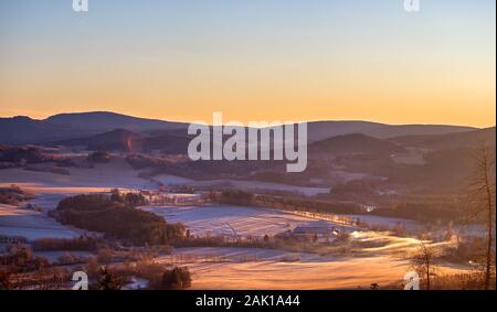 lever du soleil dans les montagnes - paysage vallonné d'hiver avec forêts, arbres et prairies (avec givre et neige) Banque D'Images