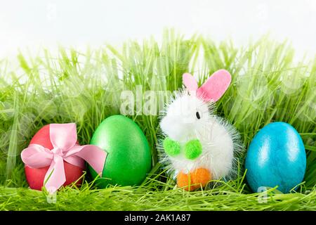 Oeufs de Pâques décorés aux couleurs vives et peu Toy Bunny sur fond d'herbe verte. Carte de Pâques. Banque D'Images