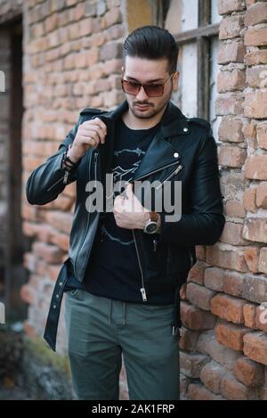 Hipster Homme avec des lunettes de soleil dans une veste debout près d'un mur de briques. Banque D'Images