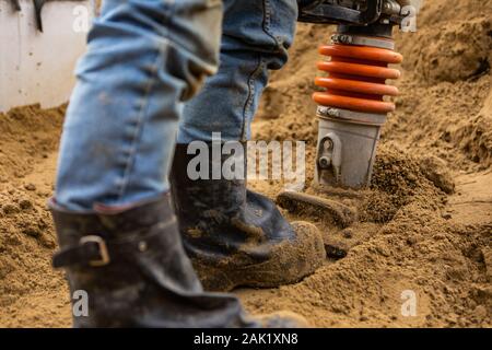 Un gros plan et selective focus shot sur les jambes d'un homme à l'aide d'un compacteur de terre lourde sur un site de construction après l'installation d'assainissement, avec copie espace Banque D'Images