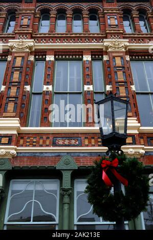Une couronne de Noël décorera une lampe à gaz devant un bâtiment commercial victorien décoré dans le quartier historique de Strand à Galveston, Texas. Banque D'Images