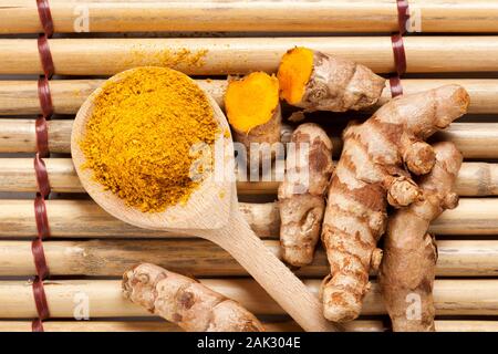 Rez-de curcuma sur cuillère en bois et des rhizomes sur des panneaux de nattes de bambou, d'en haut Banque D'Images