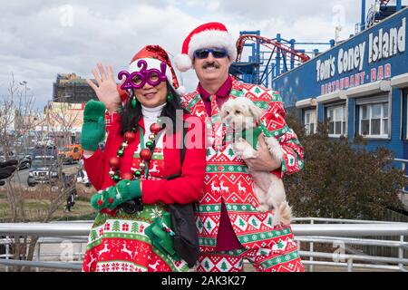 Posée portait d'un couple et leur chien laid dans des tenues de Noël sur la promenade à Coney Island le jour de l'ours polaire New Years day nager. Banque D'Images