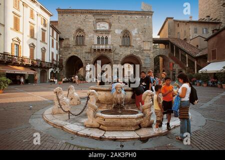 Les touristes debout à la fontaine en marbre, c'est entourée de huit lions. Il est situé en face du Palazzo della Ragione sur la Piazza Vecchia dans Banque D'Images