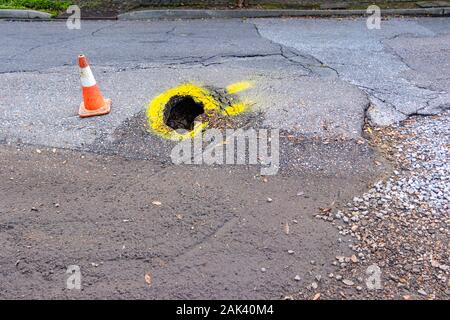 Pot trou dans la chaussée routière américaine avec la peinture jaune d'avertissement et traffic cone Banque D'Images