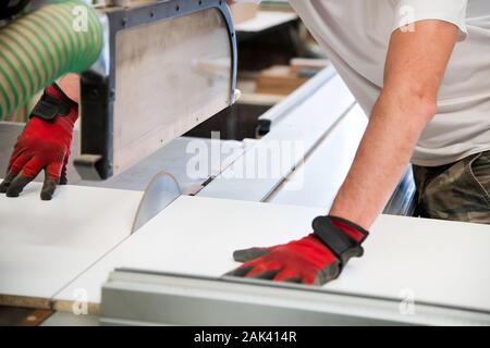 Les mains d'un charpentier en utilisant une scie circulaire dans un atelier de guider une planche de bois passé la lame Banque D'Images