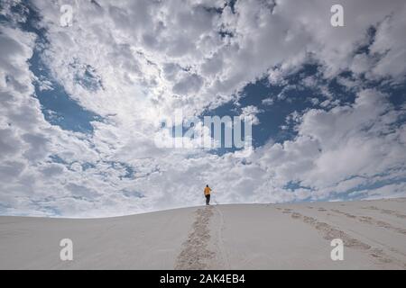 Vue arrière d'un homme en jaune t-shirt debout sur une dune de sable dans la distance contre ciel dramatique Banque D'Images