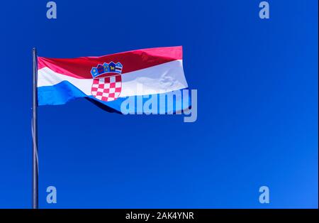 Le drapeau national croate, ou tricolore, est complètement ouvert contre un ciel bleu vif. Le manteau croate des armes est clairement visible Banque D'Images